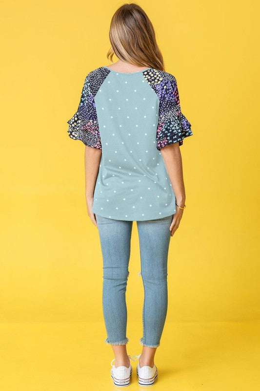 Against a vibrant yellow background, a woman with flowing long hair models the Polka Dot Print Ruffle Sleeve Top, elegantly paired with jeans.