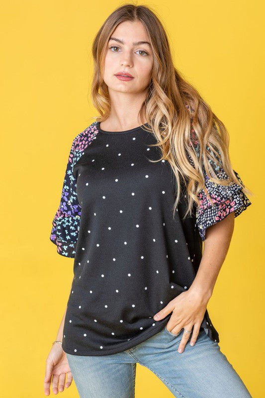 Against a vibrant yellow background, a woman with flowing long hair models the Polka Dot Print Ruffle Sleeve Top, elegantly paired with jeans.