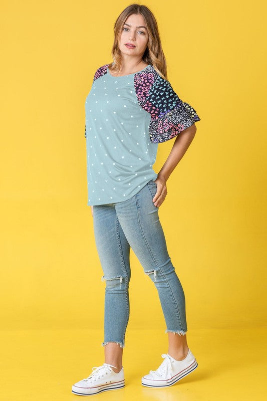 Against a vibrant yellow background, a woman with flowing long hair models the Polka Dot Print Ruffle Sleeve Top, elegantly paired with jeans.