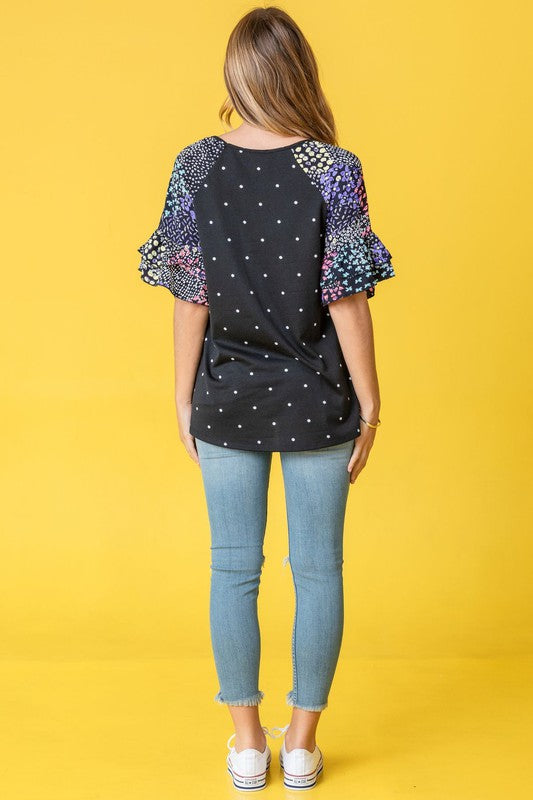 Against a vibrant yellow background, a woman with flowing long hair models the Polka Dot Print Ruffle Sleeve Top, elegantly paired with jeans.