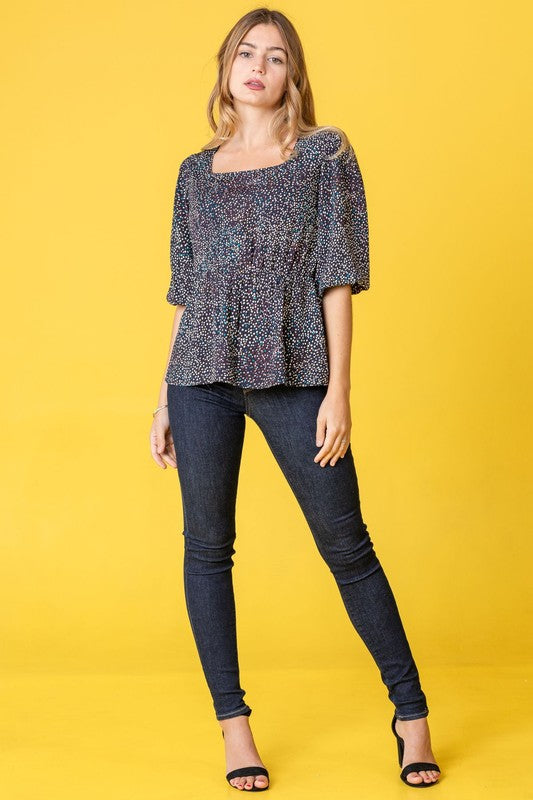 A woman with long dark hair is wearing a Plus Polka Dot Square Neck Peplum Top and blue jeans, standing in front of a beige curtain.