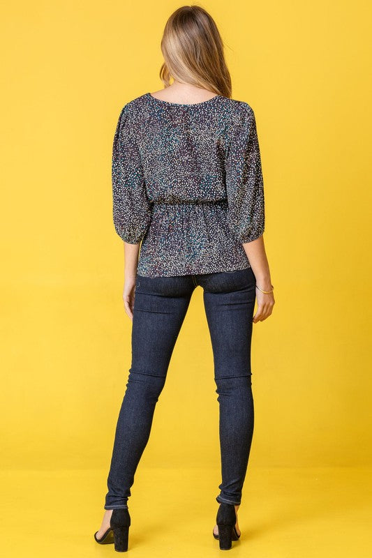 A woman with long dark hair is wearing a Plus Polka Dot Square Neck Peplum Top and blue jeans, standing in front of a beige curtain.