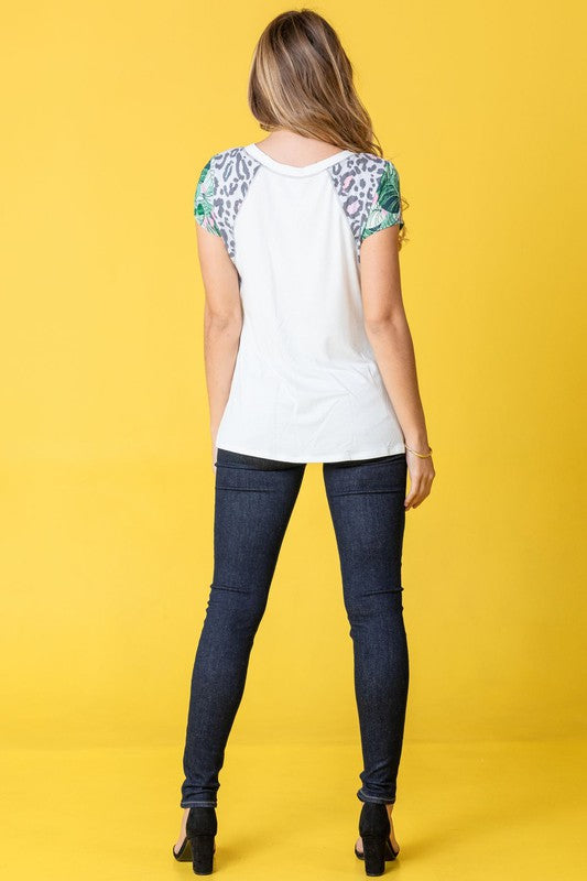 A woman stands against a yellow background, wearing the Plus Leopard Tropical Cap Sleeve Color Block Tunic paired with jeans.