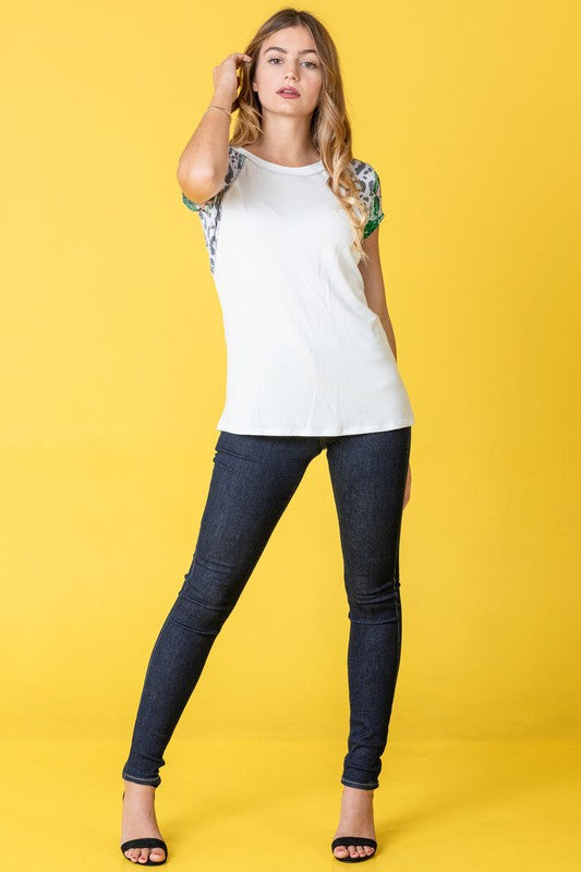 A woman stands against a yellow background, wearing the Plus Leopard Tropical Cap Sleeve Color Block Tunic paired with jeans.