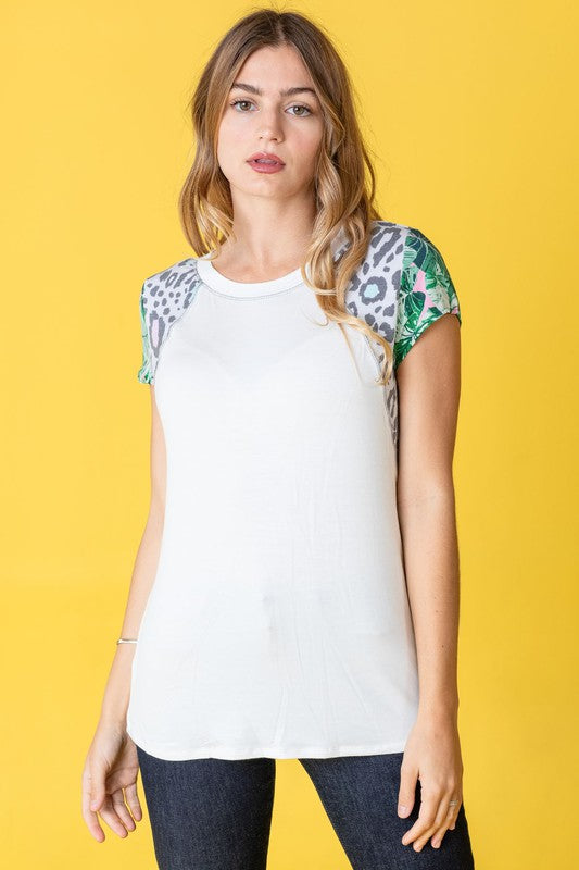 A woman stands against a yellow background, wearing the Plus Leopard Tropical Cap Sleeve Color Block Tunic paired with jeans.