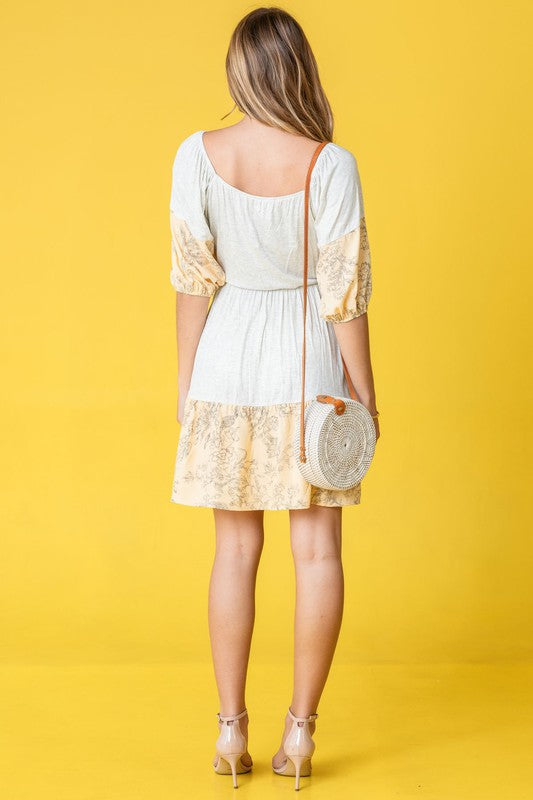 A woman wearing a Square Neck Floral Mini Dress poses elegantly against a vibrant yellow background.