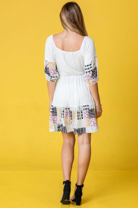 A woman wearing the Square Neck Patch Work Mini Dress poses against a yellow background.