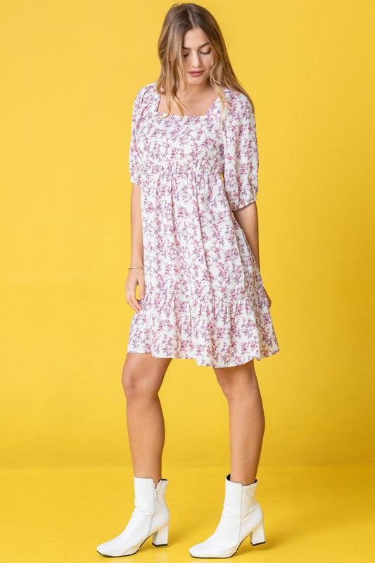 A woman wearing the Ditsy Floral Squared Neck Mini Dress and white sneakers stands in front of a pink curtain.