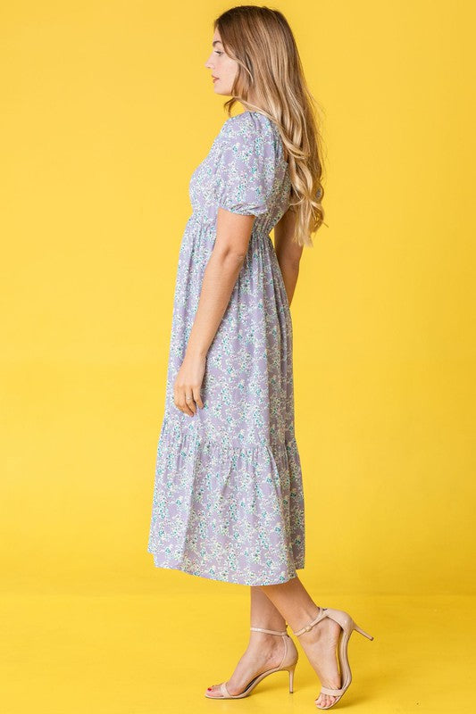 A woman in a Ditsy Floral Square Neck Sundress, crafted from 100% polyester, stands against a yellow background, highlighting its elegant light blue floral design.