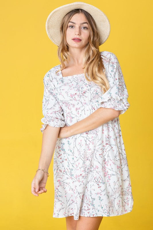 Dressed in the Branch Floral Squared Neck Mini Dress, a woman poses gracefully in front of a pink curtain.