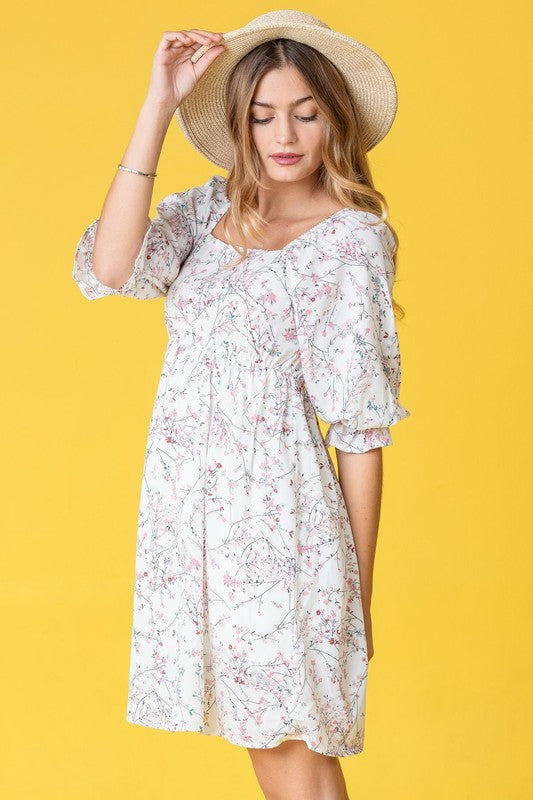 A woman in a Branch Floral Squared Neck Mini Dress and straw hat poses gracefully against a bright yellow background.