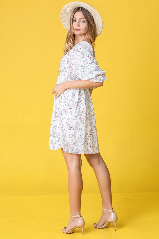 Dressed in the Branch Floral Squared Neck Mini Dress, a woman poses gracefully in front of a pink curtain.