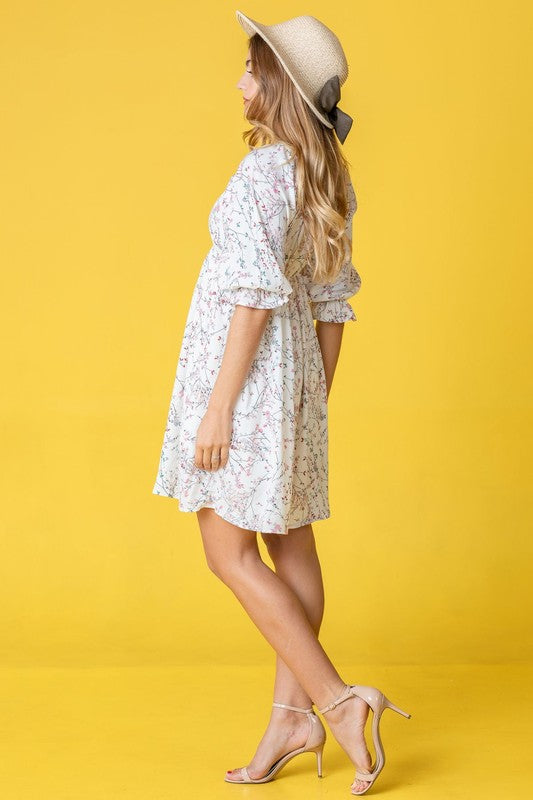 Dressed in the Branch Floral Squared Neck Mini Dress, a woman poses gracefully in front of a pink curtain.