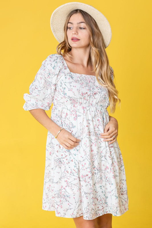 A woman in a Branch Floral Squared Neck Mini Dress and straw hat poses gracefully against a bright yellow background.