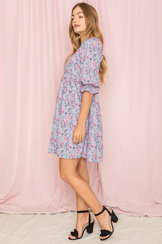 Dressed in the Branch Floral Squared Neck Mini Dress, a woman poses gracefully in front of a pink curtain.