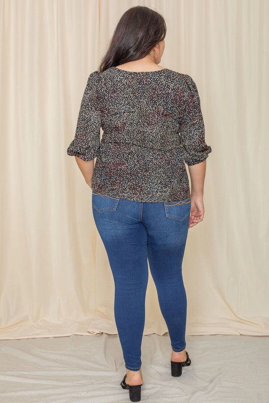 A woman with long dark hair is wearing a Plus Polka Dot Square Neck Peplum Top and blue jeans, standing in front of a beige curtain.