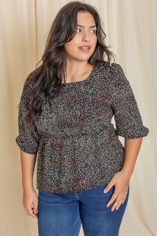 A woman with long dark hair is wearing a Plus Polka Dot Square Neck Peplum Top and blue jeans, standing in front of a beige curtain.