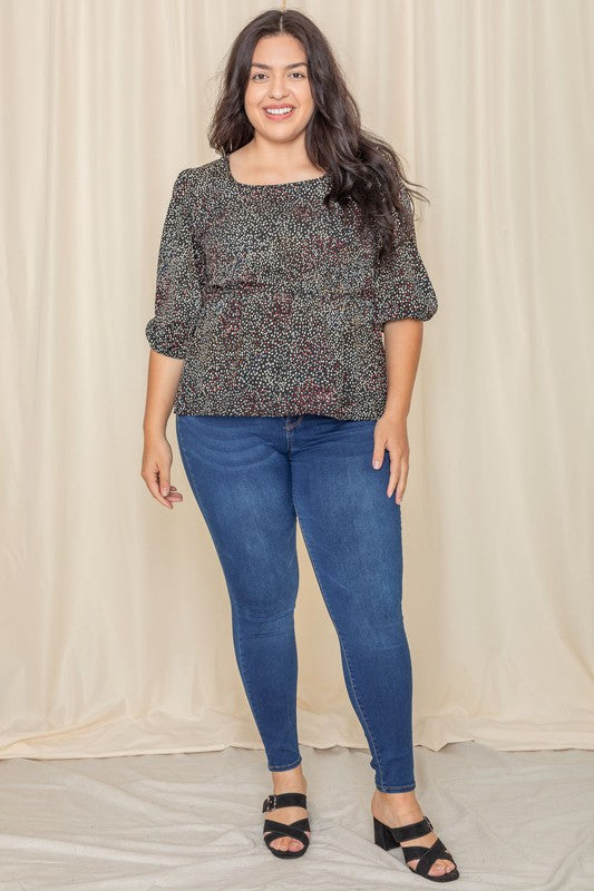 A woman with long dark hair is wearing a Plus Polka Dot Square Neck Peplum Top and blue jeans, standing in front of a beige curtain.