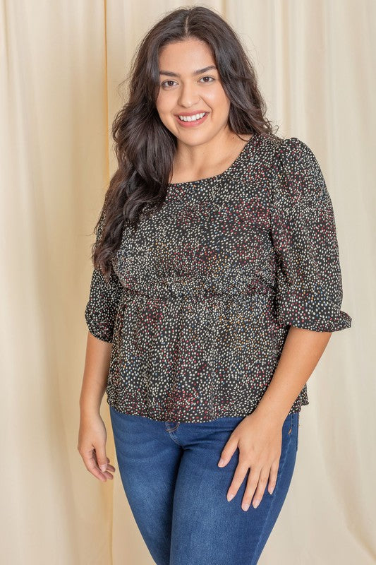 A woman with long dark hair is wearing a Plus Polka Dot Square Neck Peplum Top and blue jeans, standing in front of a beige curtain.