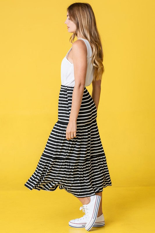 A woman in a white tank top and a Stripe Maxi Skirt stands confidently against a yellow background, accessorized with stylish white sneakers. Made in the United States, her outfit effortlessly combines comfort and elegance.