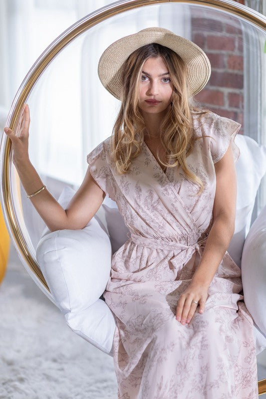 A woman in a long Floral Surplice Sash Sundress with no lining, made in the United States, stands casually in a room with contemporary furniture and large windows.