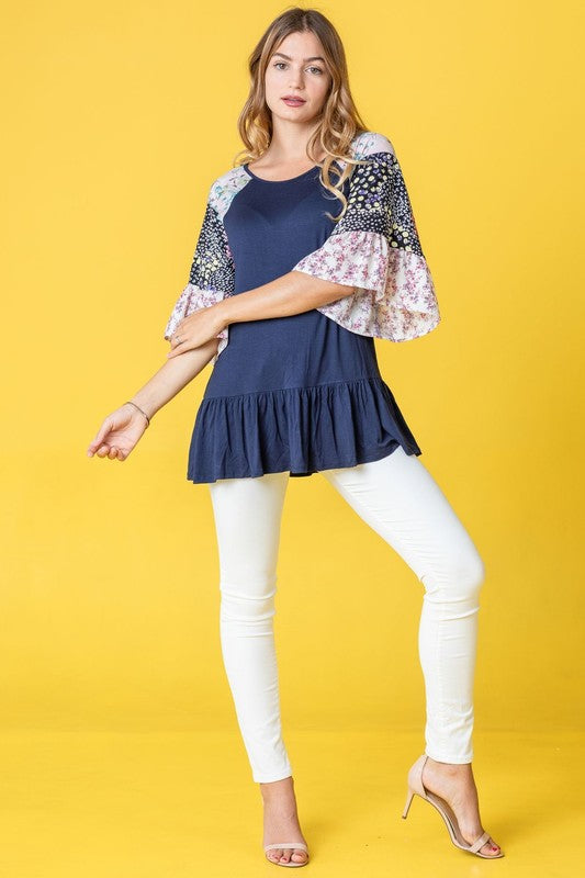 A person wearing the Plus Mix Pattern Circular Flounce Sleeve Tunic stands against a vibrant yellow background.