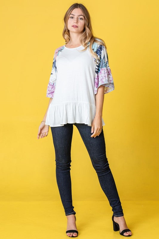 A woman stands against a yellow background wearing the Mix Pattern Circular Flounce Sleeve Tunic in navy, showcasing floral and polka dot designs on the sleeves.