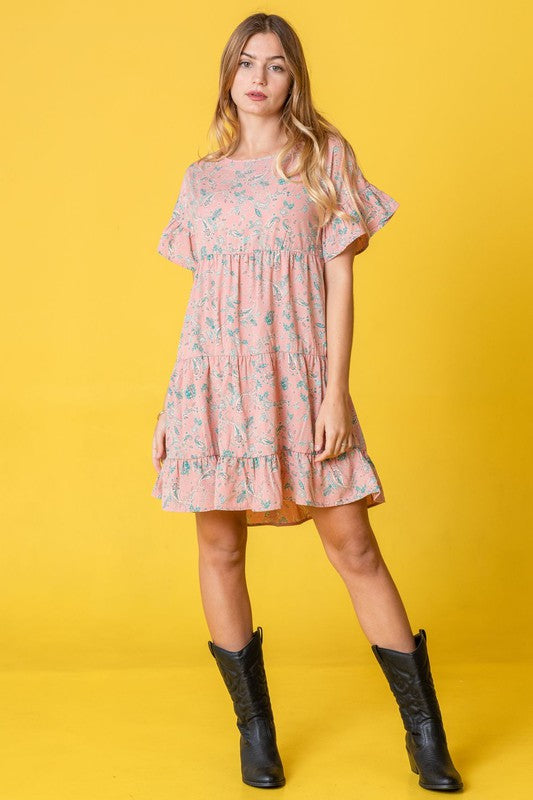 A woman in a Tiered Ruffle Trim Shift Dress stands against a pink backdrop, playfully holding a strand of her hair.