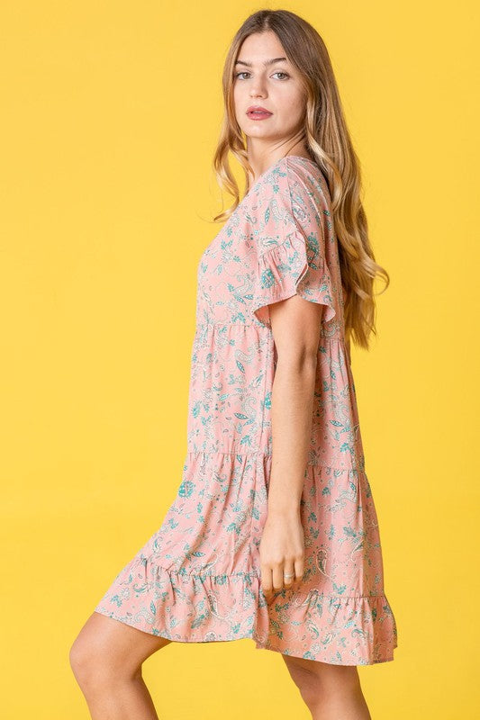 A woman in a Tiered Ruffle Trim Shift Dress stands against a pink backdrop, playfully holding a strand of her hair.