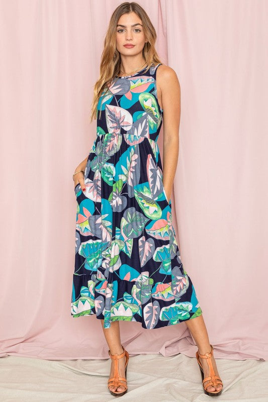 A person wearing a Sleeveless Print Ruffled Hem Tea-Length Dress stands against a pink curtain backdrop, their look reminiscent of a delicate medallion in bloom.