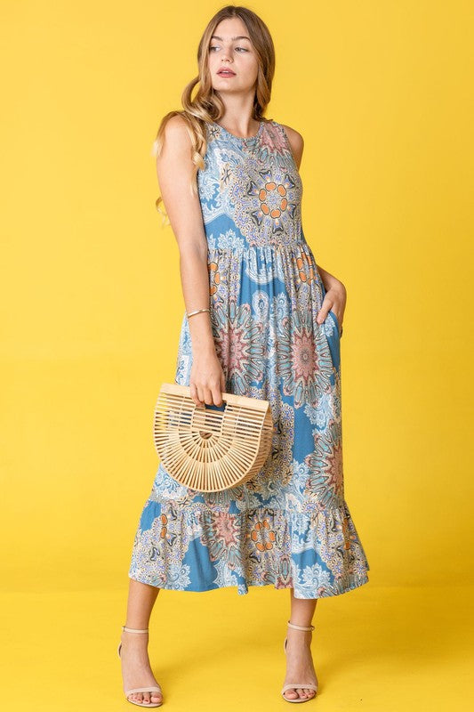 A woman in a sleeveless floral dress with a ruffled hem stands against a yellow background, holding a wooden handbag.