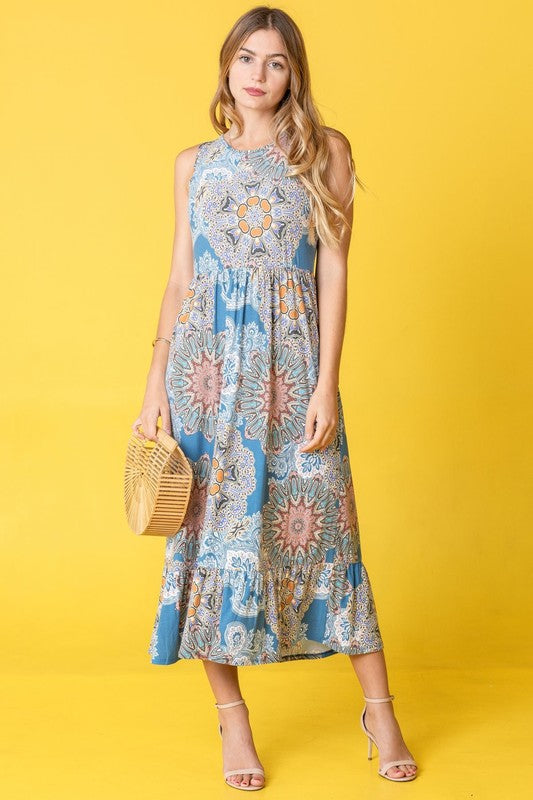 A woman in a sleeveless floral dress with a ruffled hem stands against a yellow background, holding a wooden handbag.