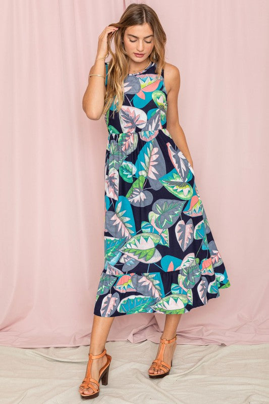 A person wearing a Sleeveless Print Ruffled Hem Tea-Length Dress stands against a pink curtain backdrop, their look reminiscent of a delicate medallion in bloom.