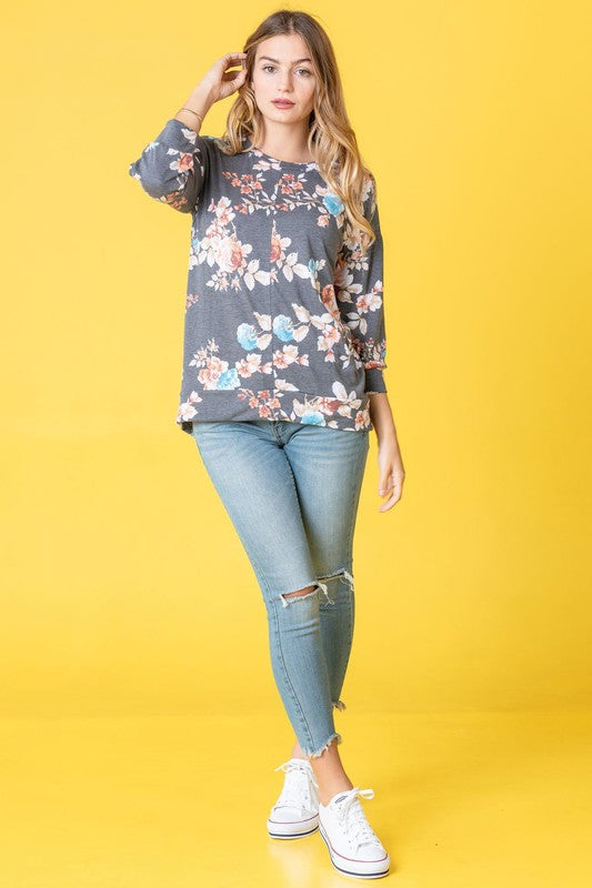 A woman wearing the Spring Floral Tunic and jeans stands against a vibrant yellow background, capturing the essence of spring.