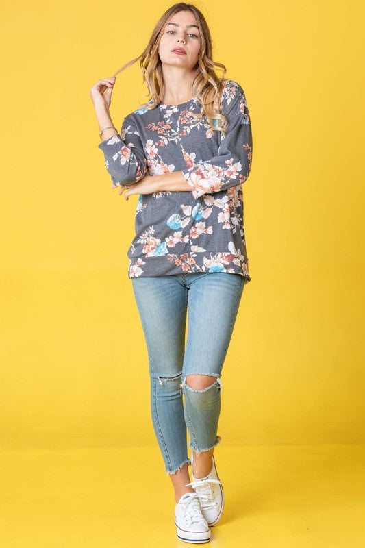 A woman wearing the Spring Floral Tunic and jeans stands against a vibrant yellow background, capturing the essence of spring.