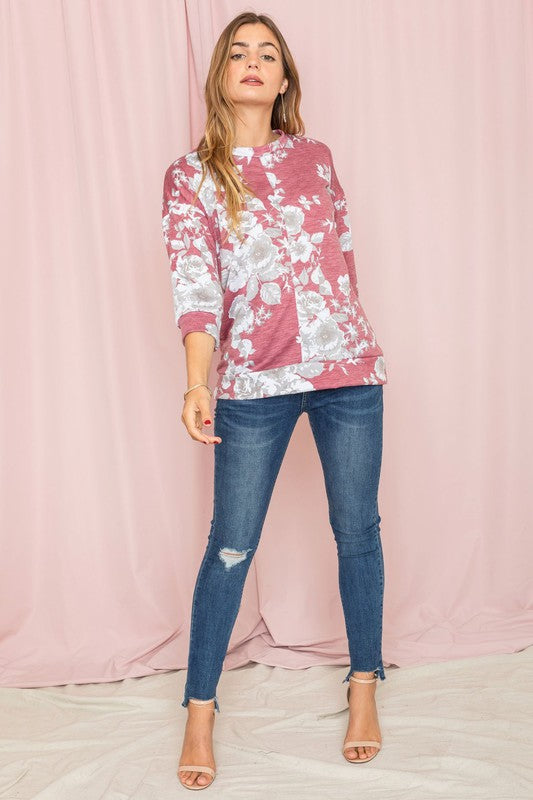 A woman wearing the Spring Floral Tunic and jeans stands against a vibrant yellow background, capturing the essence of spring.