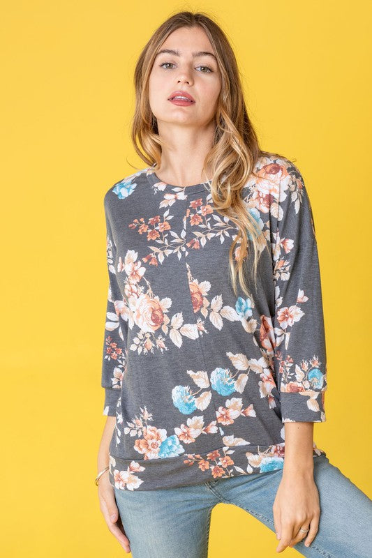 A woman wearing the Spring Floral Tunic and jeans stands against a vibrant yellow background, capturing the essence of spring.