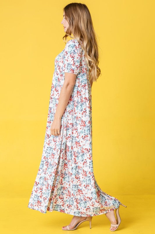 A person stands gracefully in front of a pink backdrop, wearing the Floral Square Neck Puff Sleeve dress, a blue maxi adorned with charming floral patterns.