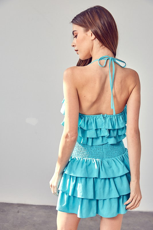 A person wearing a Smocked Waist Ruffle Romper in blue stands against a neutral background, looking directly at the camera—an ideal addition to any summer wardrobe.