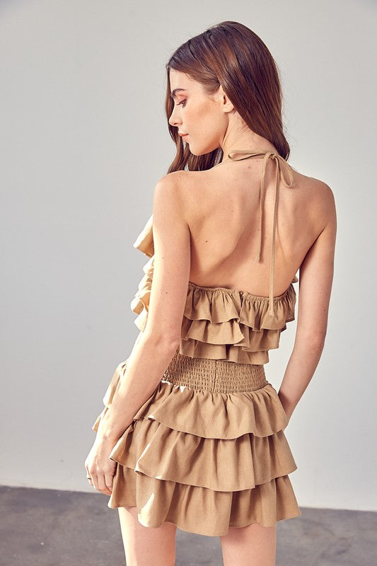 A woman wearing a beige smocked waist ruffle romper poses against a plain background.