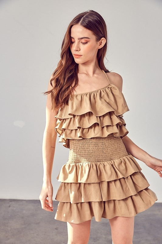 A woman wearing a beige smocked waist ruffle romper poses against a plain background.