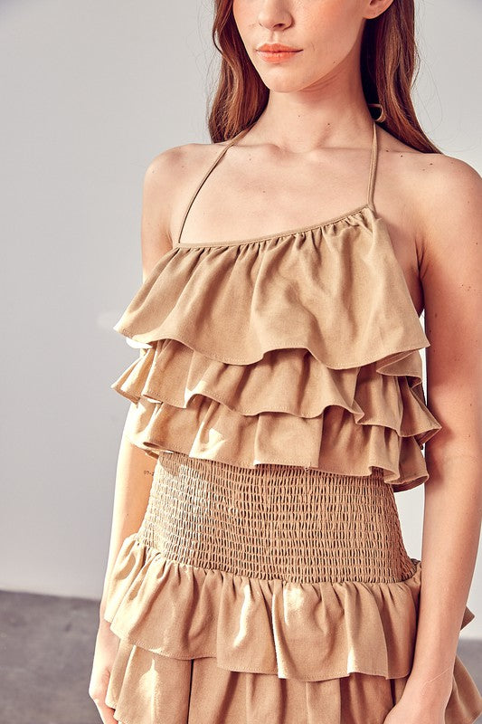 A woman wearing a beige smocked waist ruffle romper poses against a plain background.