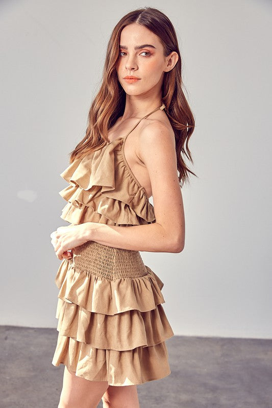 A woman wearing a beige smocked waist ruffle romper poses against a plain background.