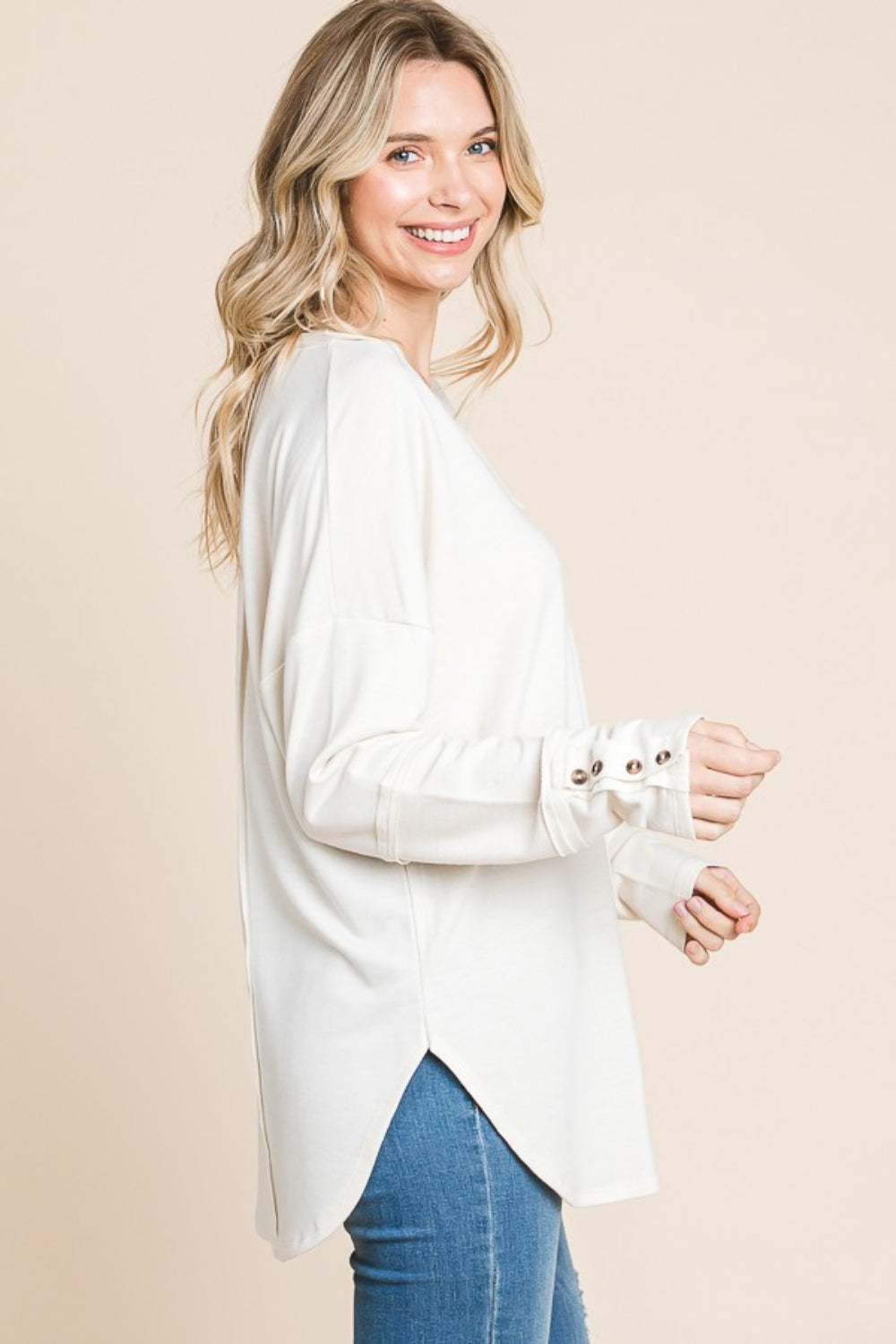 A person wearing the Culture Code Full Size V-Neck Dropped Shoulder Blouse, crafted from breathable fabric, poses against a beige background, highlighting the button details on the sleeves.