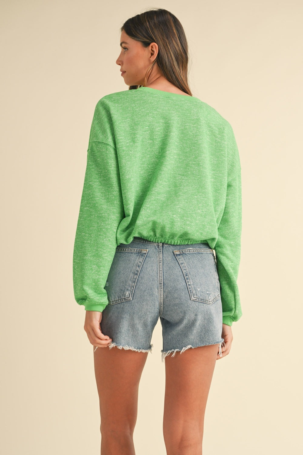 A woman models a Mable Round Neck Letter Embroidery Crop Sweatshirt in green, paired with denim shorts, against a plain background, effortlessly showcasing her street style.