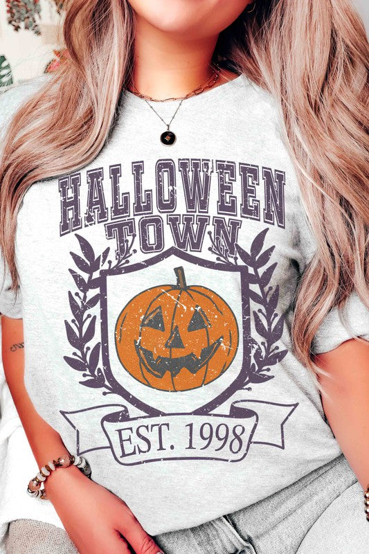 A person wearing a premium cotton HALLOWEEN TOWN Graphic Tee featuring an est. 1998 jack-o'-lantern design, displaying a peace sign with their right hand.