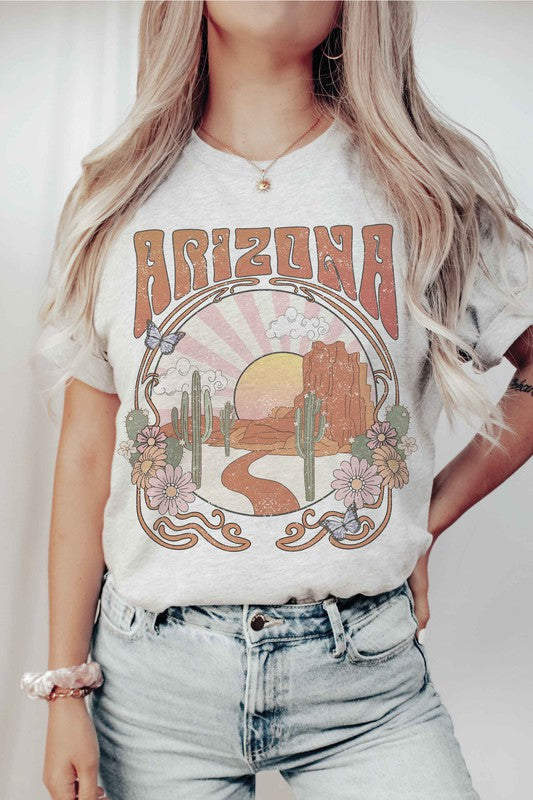 Someone wearing an ARIZONA DESERT Graphic Tee in unisex sizing, which showcases a lively desert scene with the word "Arizona," paired with light blue jeans. The tee's 100% cotton material enhances the comfort and style of this casual look.