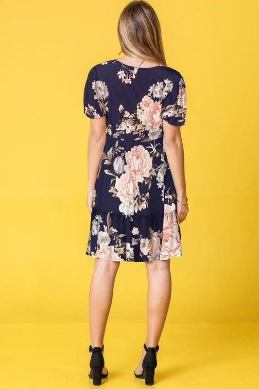 A woman in a Surplice Tiered Midi Dress stands against a vibrant yellow background, her style epitomizing the charming fashion trends of the United States.