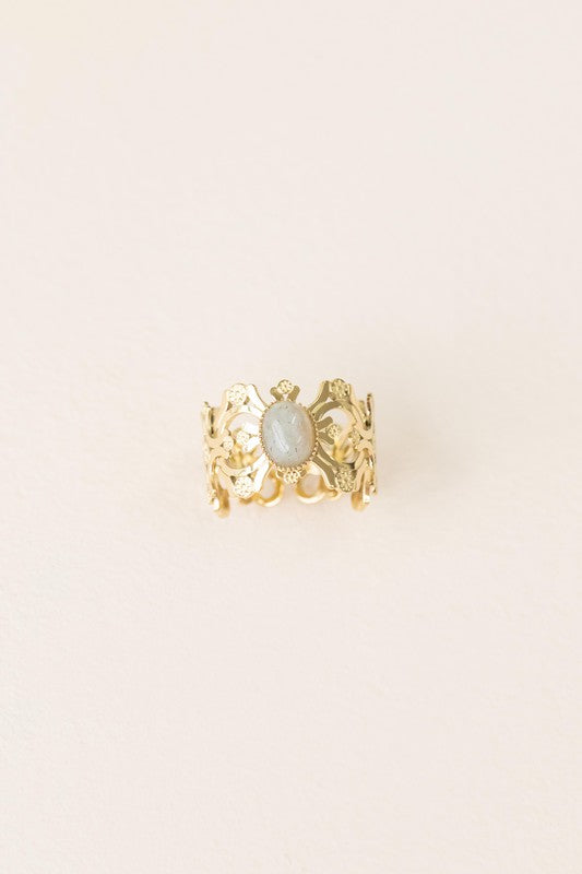 Presenting the Perdita Adjustable Ring—a bohemian treasure. This 14k gold-plated piece boasts an intricate design, highlighting a central oval gemstone beautifully set against a light background.