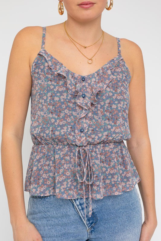 A person wearing a Sleeveless Elastic Waist Top With Ruffle, showcasing a floral pattern, paired with light blue jeans, stands against a white background.